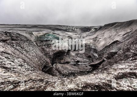 Blick auf einen faszinierenden Wasserfall, der das krasse, felsige Gelände hinunterstürzt und einen atemberaubenden Kontrast zum bewölkten Himmel schafft, Island, Island. Stockfoto