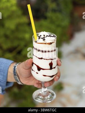Der Barista hält einen erfrischenden Milchshake mit Eiskaffee und Schlagsahne, Schokoladensirup und Schokoladenchips Stockfoto
