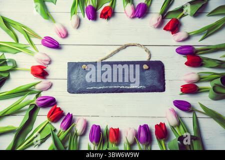 Die Abbildung zeigt ein Schild aus schwarzem Schiefer, das an grobem Garn zwischen Tulpenrand hängt Stockfoto