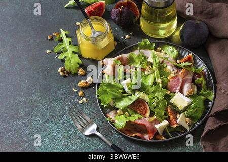 Gesundes Lebensmittelkonzept. Herbstsalat mit Feigen, Schinken, Rucola, Spinat, Käse, Walnüsse und Honig auf einer Steinplatte. Kopierbereich Stockfoto