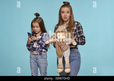 Charmante blonde Mädchen und schöne Kind mit einer lustigen Frisuren, in den weißen T-Shirts gekleidet, karierten Hemden und Blue Denim Jeans stellen gegen eine Blu Stockfoto