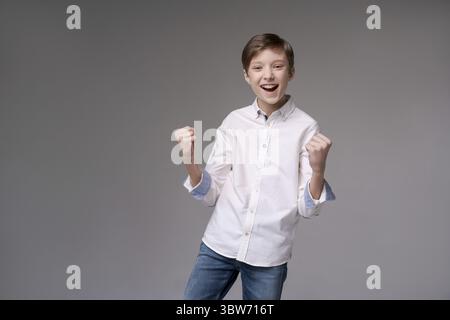 Ich habe gewonnen. Glücklicher Mann feiert den Sieger in weißem Hemd. Dynamisches Bild kaukasischer männlicher Teenager auf grauem Studiohintergrund. Victory adm Stockfoto