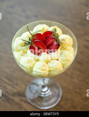 Zitronenmousse-Dessert in einem Cocktailglas auf einem Holztisch, dekoriert mit frischen Erdbeeren Stockfoto