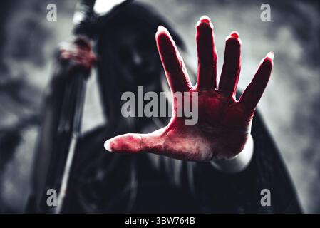 Hexe, die blutige Hand mit Reaper. Weiblicher Dämon Engel in schwarzer Kleidung und Haube auf grunge Wand Hintergrund. Halloween Tag und Geheimnis, das Konzept. Fant Stockfoto