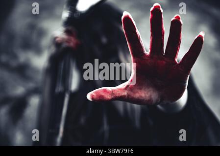 Hexe, die blutige Hand mit Reaper. Weiblicher Dämon Engel in schwarzer Kleidung und Haube auf grunge Wand Hintergrund. Halloween Tag und Geheimnis, das Konzept. Fant Stockfoto