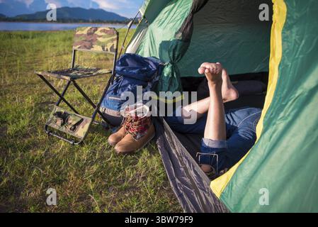 Nahaufnahme von Frau Beine entspannen in camping Zelt mit Bergsee und Wiese und Wiese Hintergrund. Lebensstile und Personen Konzept. Camping und p Stockfoto
