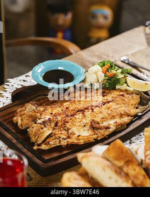 Gegrillter Flunder-Fisch mit Gemüse auf Holzteller mit einer Schüssel Sojasauce auf einem Tisch für eine Mahlzeit serviert Stockfoto