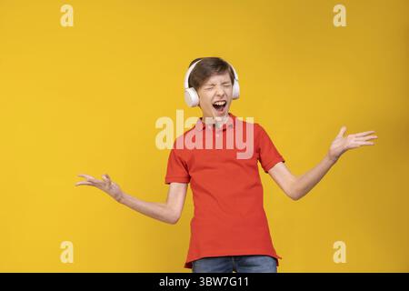 Portrait lustiger gutaussehender kaukasier in rotem T-Shirt, Musik in Kopfhörern hören, herumtäuschen und mit glücklichem Gesichtsausdruck tanzen, Hand Stockfoto