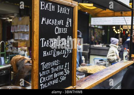 Essensmarktstand mit einem Tafel-Menü und Gästen, die frische lokale Küche in lebhafter Umgebung stöbern Stockfoto