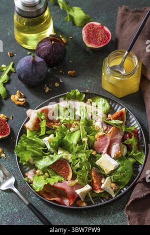 Gesundes Lebensmittelkonzept. Herbstsalat mit Feigen, Schinken, Rucola, Spinat, Käse, Walnüsse und Honig auf einer Steinplatte Stockfoto