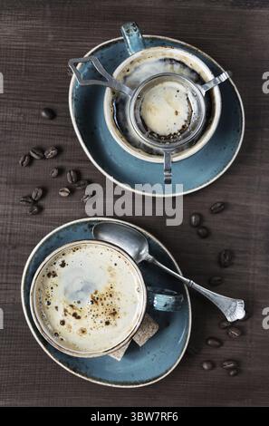 Zwei Tassen Kaffee, Kaffeebohnen, Zuckerstücke und Teelöffel auf einem Holztisch, Blick von oben Stockfoto