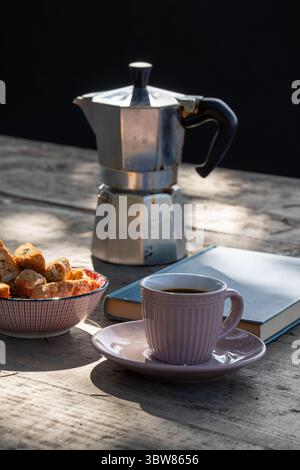 Authentische italienische Kaffeepausen-Szene mit einer traditionellen Mokakanne, einer Tasse frischen Espresso, Biscotti und einem Buch auf einem rustikalen Holztisch Stockfoto