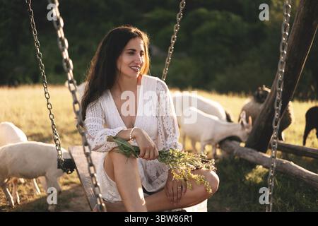 Wunderschönes Sommerportrait einer Schönheit in einem weißen Kleid, das im Gras sitzt und die Natur genießt Stockfoto