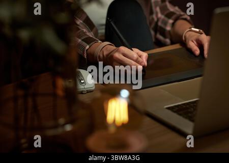 Weibliche Hände mit Grafiktablett-Retuschierung auf Laptop-Computer bei Nacht Stockfoto