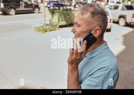 Ein Seniorenmann mit einer Hörbehinderung benutzt im Alltag ein Hörgerät und spricht im Freien in der Stadt. Hörlösungen Stockfoto