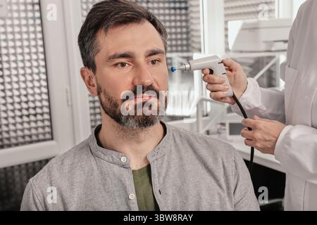Porträt des gutaussehenden Mannes bei Tympanometrie und Mittelohrfunktionsprüfung mit HNO-Arzt mit Tympanometersonde am Hörzentrum, Nahaufnahme Stockfoto