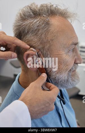Hörlösungen. Audioprothetist passt die Hörgeräte älterer Patienten mit speziellen Geräten an und nimmt echte Ohrmessungen an Stockfoto