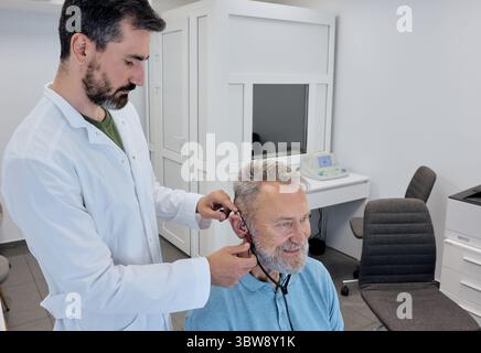 Der Audiologe passt ein Hörgerät fachmännisch mit spezieller Ausrüstung an, um eine bessere Anpassung des Seniorenpatienten zu gewährleisten. Individuelle Hörgeräteanpassung Stockfoto