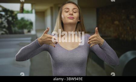 Frau genießt friedliche Momente im Freien mit geschlossenen Augen und in beruhigender Geste erhobenen Händen und trägt ein lässiges lila Top in ruhiger Umgebung. Stockfoto