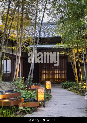 Ruhiger japanischer Gartenweg in der Abenddämmerung, beleuchtete Laternen führen zu einem traditionellen Haus mit Shoji-Bildschirmen. Bambus umgibt die ruhige Szene. Peacefu Stockfoto