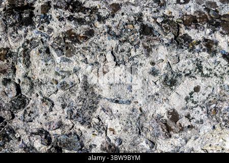 Raue Betonoberfläche mit verwitterter Textur. Nahaufnahme einer verwitterten Betonoberfläche mit rauer Textur, eingebetteten Steinen und natürlichen Rissen Stockfoto