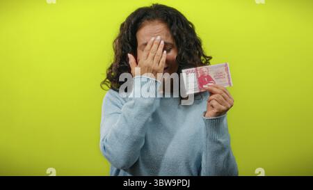 Eine Frau, die isländische Krone hält, scheint vor einem hellgelben Hintergrund besorgt zu sein. Stockfoto