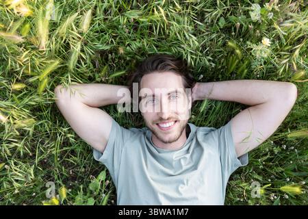 Porträt eines entspannten Mannes, der auf grünem Gras liegt, von oben gesehen Stockfoto