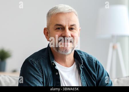 Schöner grauhaariger älterer Mann, der im Wohnzimmer auf der Couch posiert Stockfoto