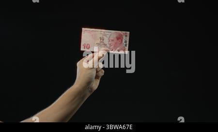 Mann hält die türkische Lira-Banknote vor schwarzem isoliertem Hintergrund in der Hand und hebt Währungs- und Finanzthemen mit Schwerpunkt auf Details und Textur hervor Stockfoto