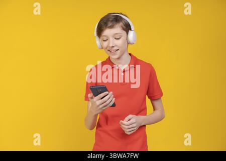 Portrait junger Mann, der Musik mit Kopfhörern auf gelbem Hintergrund in einem Studio mit rotem T-Shirt und Jeans hört. Kaukasischer Teenager tanzt und Stockfoto
