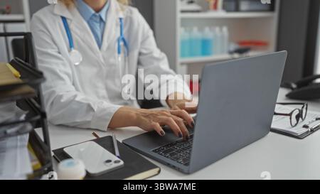 Ärztin mittleren Alters, die an einem Laptop in einem Krankenhauszimmer arbeitet, konzentriert sich auf Aufgaben mit medizinischen Geräten in einer klinischen Umgebung, Hand-on-Keybo Stockfoto