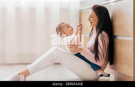 Frau Mutter, die das Baby hält, während sie auf dem Boden sitzt Stockfoto