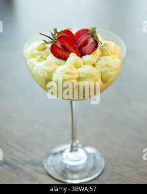 Köstliches cremiges Dessert mit frischen Erdbeeren wird in einem eleganten Glas auf einem Holztisch serviert Stockfoto