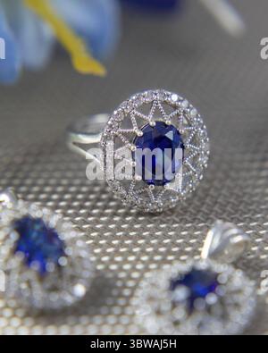 Silberring mit einem großen blauen Edelstein und kleinen Diamanten umgeben von anderem Schmuck auf grauer Oberfläche Stockfoto