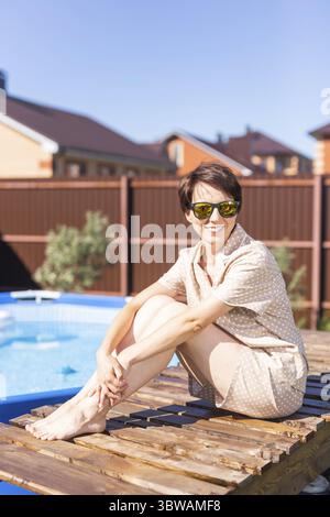 Portrait einer hübschen jungen Frau im Pyjama, die in der Nähe eines aufblasbaren Schwimmbades sitzt - Sommer- und Landleben-Konzept Stockfoto