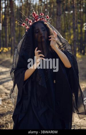 Schöne, böse, langhaarigen Charmeur in einem schwarzen, langen besticktes Kleid. Es gibt grosse rote Krone in ihren braunen, lockiges Haar unter einem schwarzen Schleier. Sie i Stockfoto
