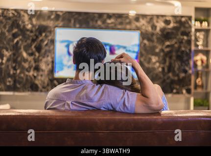 Asiatische junge Geliebte Fernsehen auf Sofa. Paare und Entspannen. Urlaub und Ferienhäuser Konzept. Nacht dating und Flitterwochen Thema. Ansicht von hinten Stockfoto