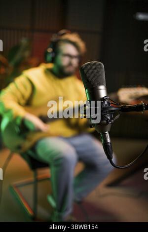 Männlicher Sänger, der Songs mit einem Studiomikrofon aufnimmt und Gitarre in einem Musikstudio spielt. Performance und Show im Musikgeschäft Stockfoto