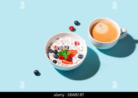 Gesundes Frühstück mit Chia Schüssel und Cappuccino Kaffee auf blauem Hintergrund, trendiges Design mit hartem Licht. Chia Pudding mit Beeren. Gesunde Pflanzenböden Stockfoto
