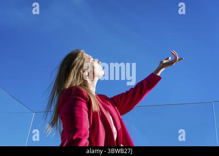 Eine Frau in einer roten Jacke schaut in den Himmel. Der Himmel ist blau und klar, und die Frau ist in kontemplativer Stimmung Stockfoto