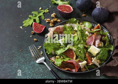 Gesundes Lebensmittelkonzept. Herbstsalat mit Feigen, Schinken, Rucola, Spinat, Käse, Walnüsse und Honig auf einer Steinplatte. Kopierbereich Stockfoto