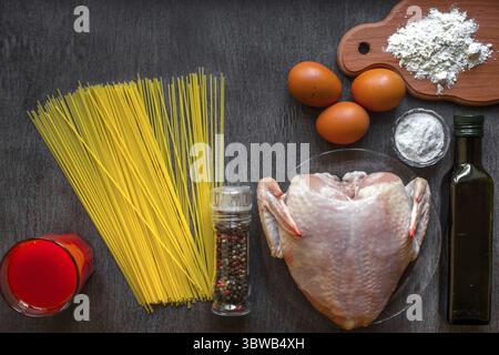 Gekochte Spaghetti-Nudeln. Ungekochte Spaghetti und rohes Huhn an Bord. Zutaten für hausgemachte Nudeln Hühnereier, Pflanzenöl. Die dunkelschwarze w Stockfoto