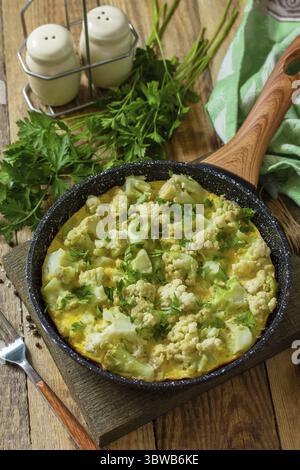 Diätfrühstück oder gesundes Mittagessen. Eieromelett mit Blumenkohl in einer gusseisernen Pfanne auf rustikalem Holztisch Stockfoto