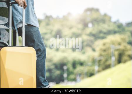 Nahaufnahme der Mann Beine während der Fahrt auf Road Trip mit gelben Koffer auf Sommer Natur Hintergrund ruht. Transport und Menschen Lebensstile Konzept. Stockfoto