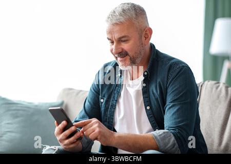 Lächelnder älterer Mann mit Smartphone zu Hause Stockfoto