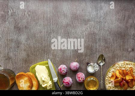 Haferflocken mit Pflaumen, Toast mit Butter und Honig auf einem Holztisch. Eine Tasse schwarzen Tee. Das Konzept eines gesunden Frühstücks. Draufsicht. Speicherplatz kopieren. Still Stockfoto