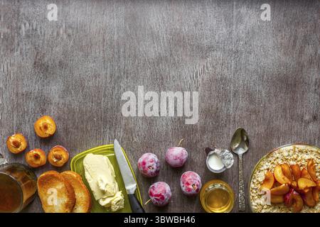 Haferflocken mit Pflaumen, Toast mit Butter und Honig auf einem Holztisch. Eine Tasse schwarzen Tee. Das Konzept eines gesunden Frühstücks. Draufsicht. Speicherplatz kopieren. Still Stockfoto