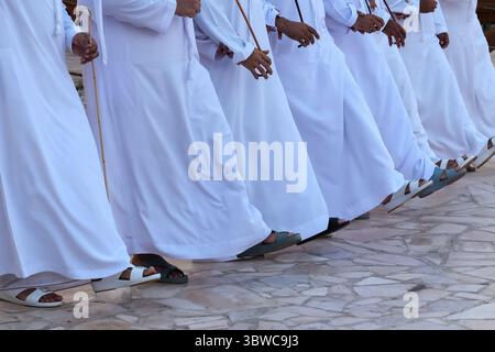 Niedrigwinkelaufnahme der Füße von Männern aus Emiraten in weißen Thoben, die Folk-Al-Ayyala-Tanz, rhythmische Bewegungen und traditionelle Schuhe aufführen. Stockfoto