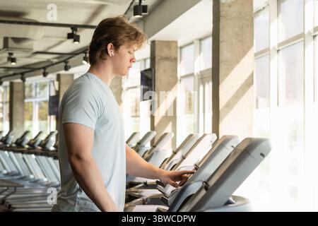 Athlet Mann mit blauem T-Shirt Laufbahn, Aufwärmen auf Laufband im Fitnessstudio. Auswahlprogramm. Nahaufnahme. Stockfoto