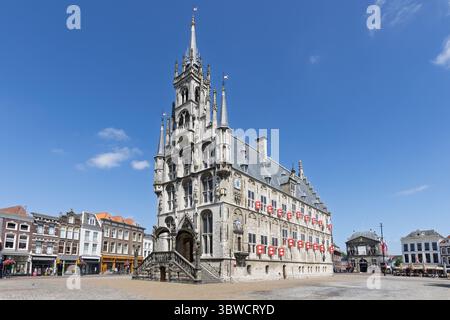 Das Grand Gouda Rathaus dominiert den Marktplatz unter einem klaren blauen Himmel, ein atemberaubendes Beispiel für niederländische gotische Architektur. Stockfoto